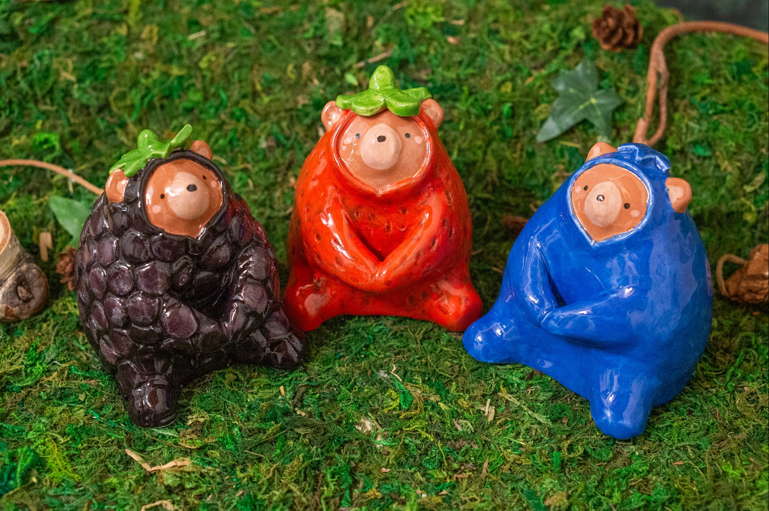 Three small figurines of bears in colorful berry outfits on a green textured surface.